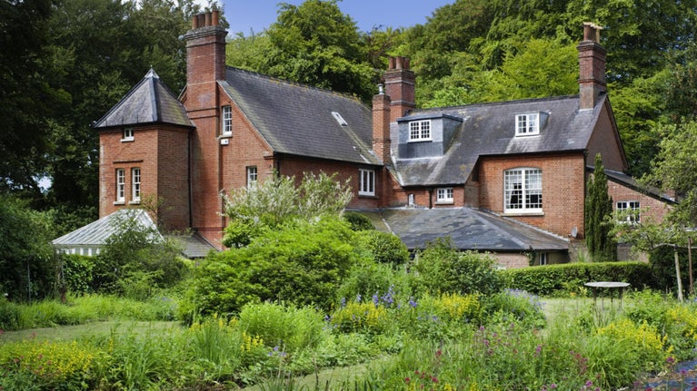 A large detached, red brick Victorian home in summer. The garden is in bloom in the foreground.